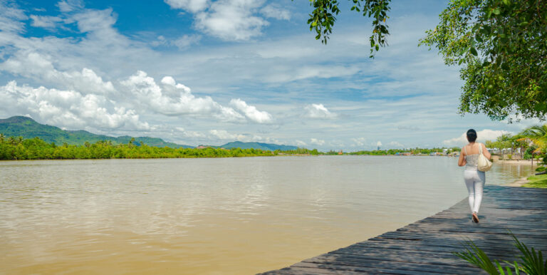 Guest walking along riverside at Kampot resort with wide river and natural landscape – hotel photography Cambodia