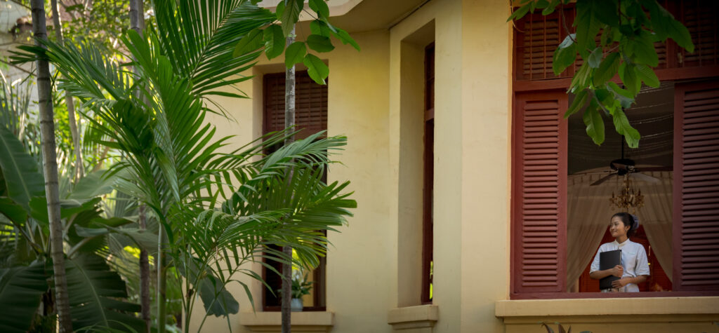 staff member looking out of window of colonial building at la rivere dangkor boutique hotel in siem reap